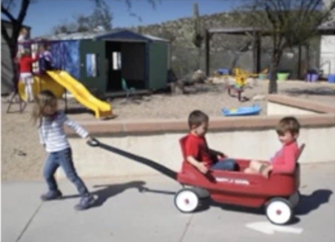 Children pulling a red wagon on the preschool playground.